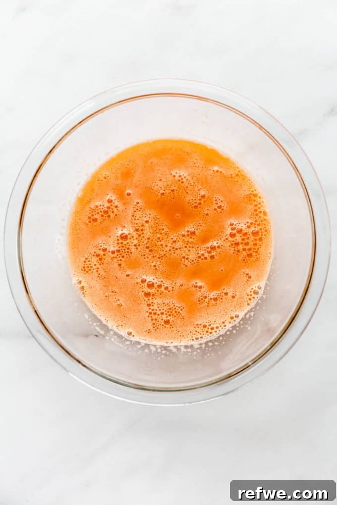 Zingy Ginger Carrot Orange Immunity Nectar 7 A clear mixing bowl filled with the vibrant, freshly strained orange, carrot, and ginger juice, sparkling with freshness.