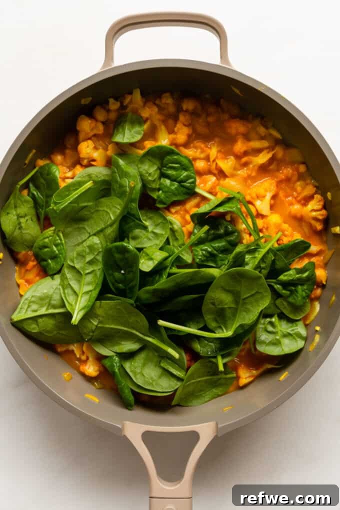 Golden Cauliflower Chickpea Curry 7 cauliflower curry and fresh spinach leaves in a pan