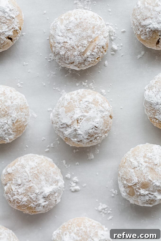 A close-up of an almond snowball cookie being rolled in a bowl of powdered sugar for its second, final coating.