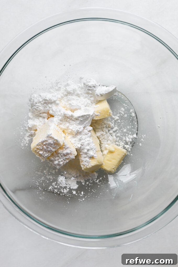 Softened butter and powdered sugar sitting in a clear glass mixing bowl, ready to be creamed.