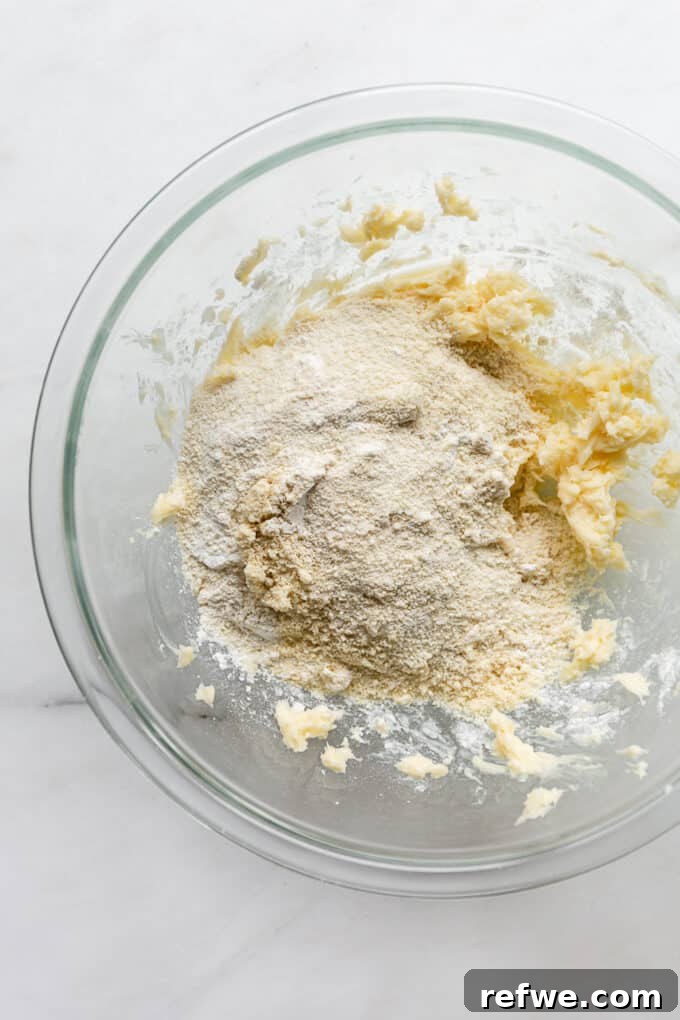 Almond flour and salt added to the butter and sugar mixture in a bowl, ready to be combined into dough.
