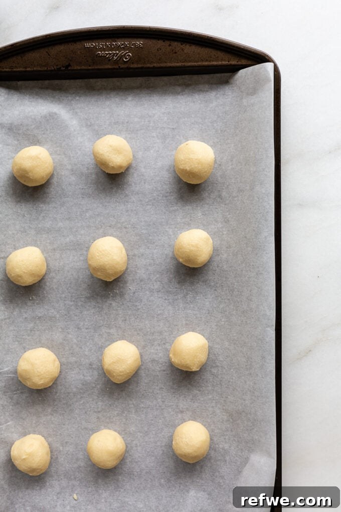 Small, uniformly rolled almond snowball cookie dough balls arranged on a parchment-lined baking sheet before baking.