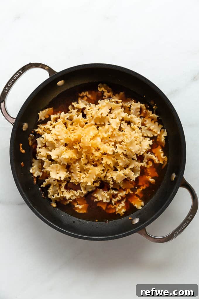 Creamy French Onion Pasta Skillet 7 Uncooked pasta and broth simmering together in a pot, absorbing liquid.
