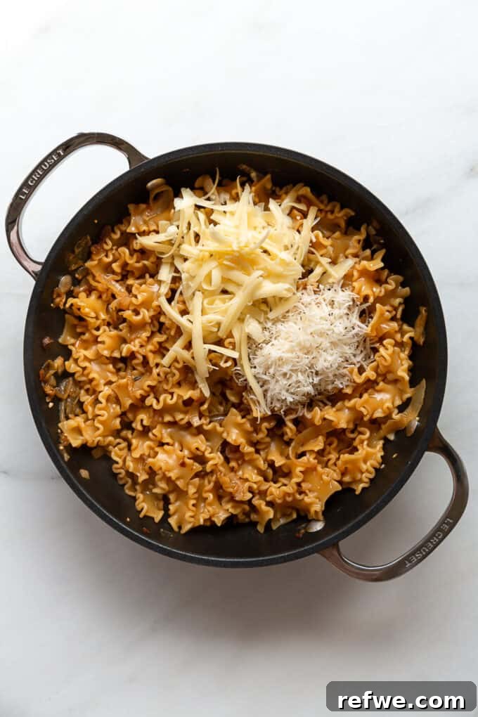 Creamy French Onion Pasta Skillet 8 Shredded Gruyere and Parmesan cheese being stirred into the cooked pasta to create a creamy sauce.