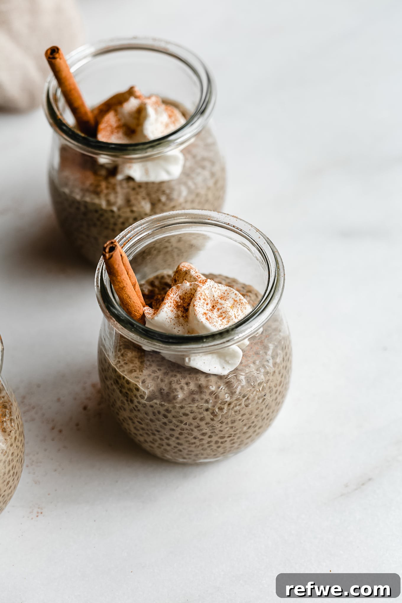 Gingerbread Spice Chia Delight 7 Two jars of gingerbread chia pudding, beautifully garnished with whipped cream and a sprinkle of cinnamon, against a warm, festive background.