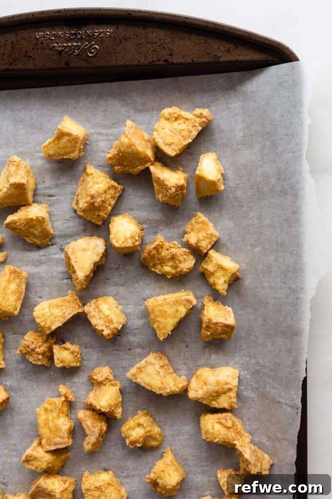 Gochujang Glazed Tofu 5 Crispy, golden-brown tofu cubes spread evenly on a baking sheet after being baked.