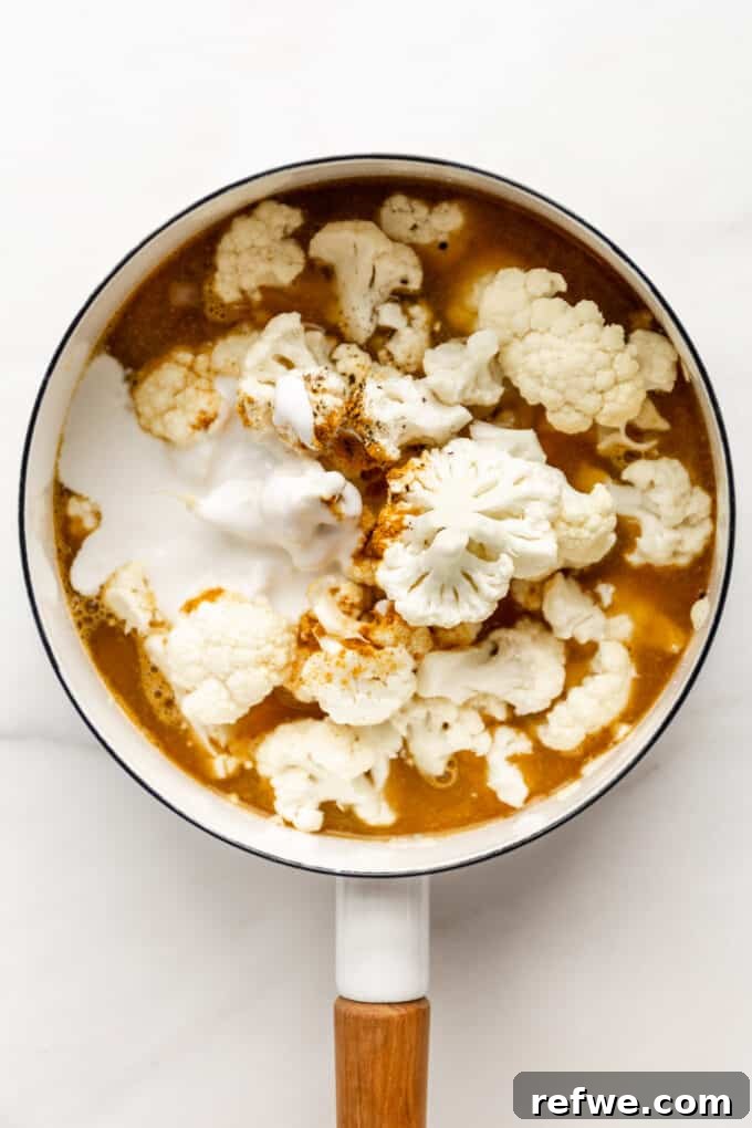 Velvety Curried Cauliflower Bliss 6 Vegetable broth and full-fat coconut milk being poured over the cauliflower and spices in the pot.
