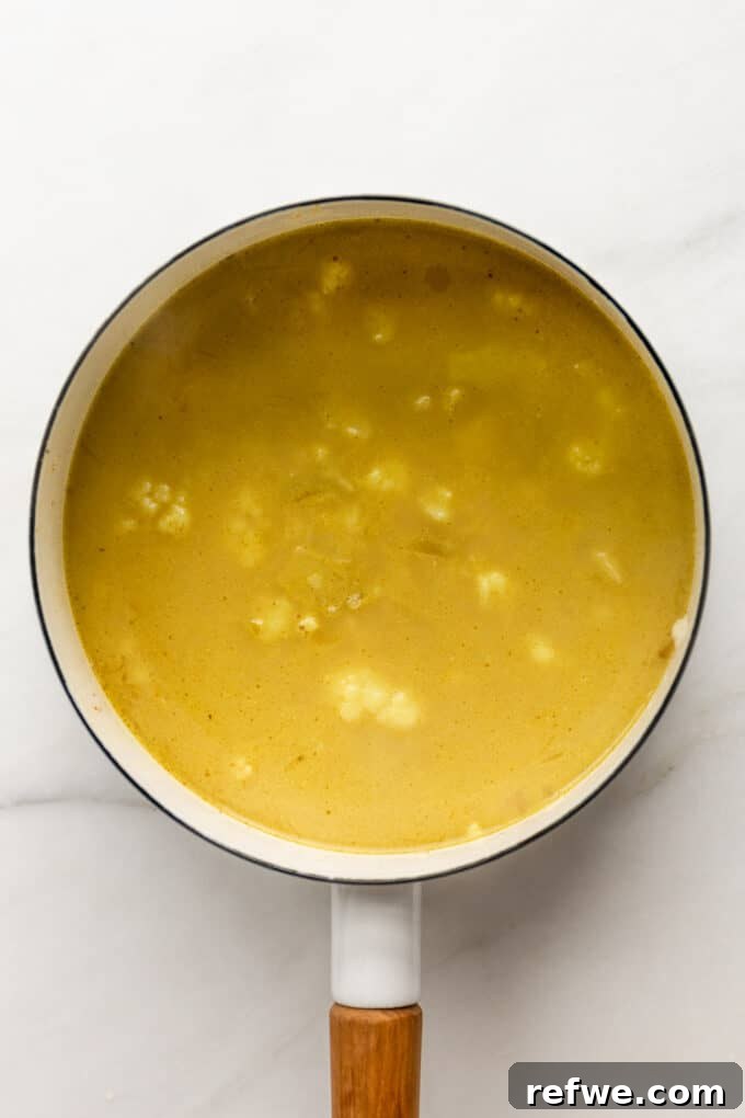 Velvety Curried Cauliflower Bliss 7 Unblended cauliflower soup simmering gently in a white pot, with tender cauliflower florets visible.
