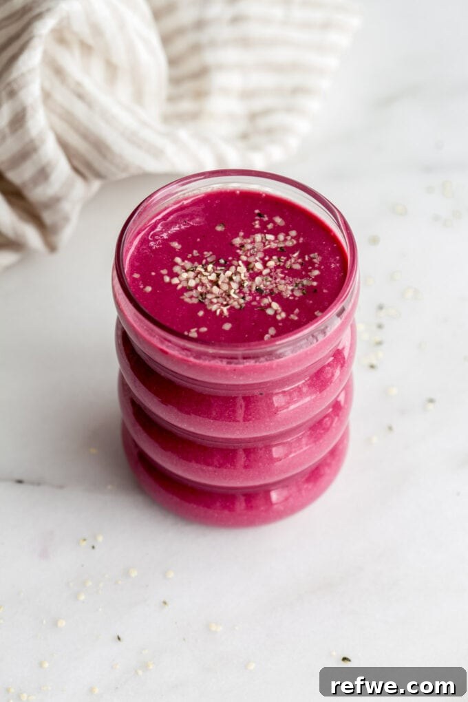 A beautifully prepared beet smoothie in a glass, topped with a sprinkle of hemp seeds, resting on a marble counter.