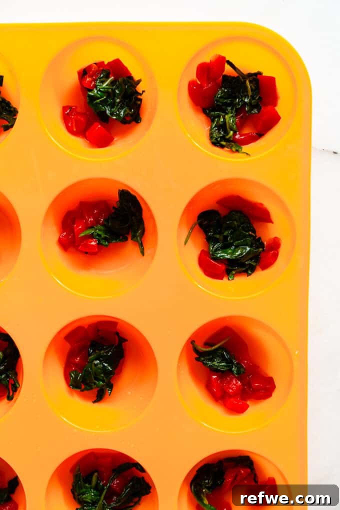 Lean Protein Egg Cups 5 Roasted red peppers and wilted spinach artfully arranged in the cups of an orange silicone muffin pan.