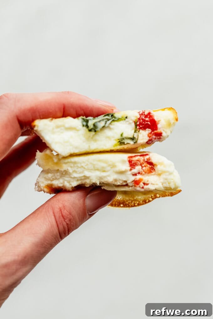 Lean Protein Egg Cups 9 A single egg white bite cut in half, revealing its fluffy interior and colorful fillings of spinach and red pepper.