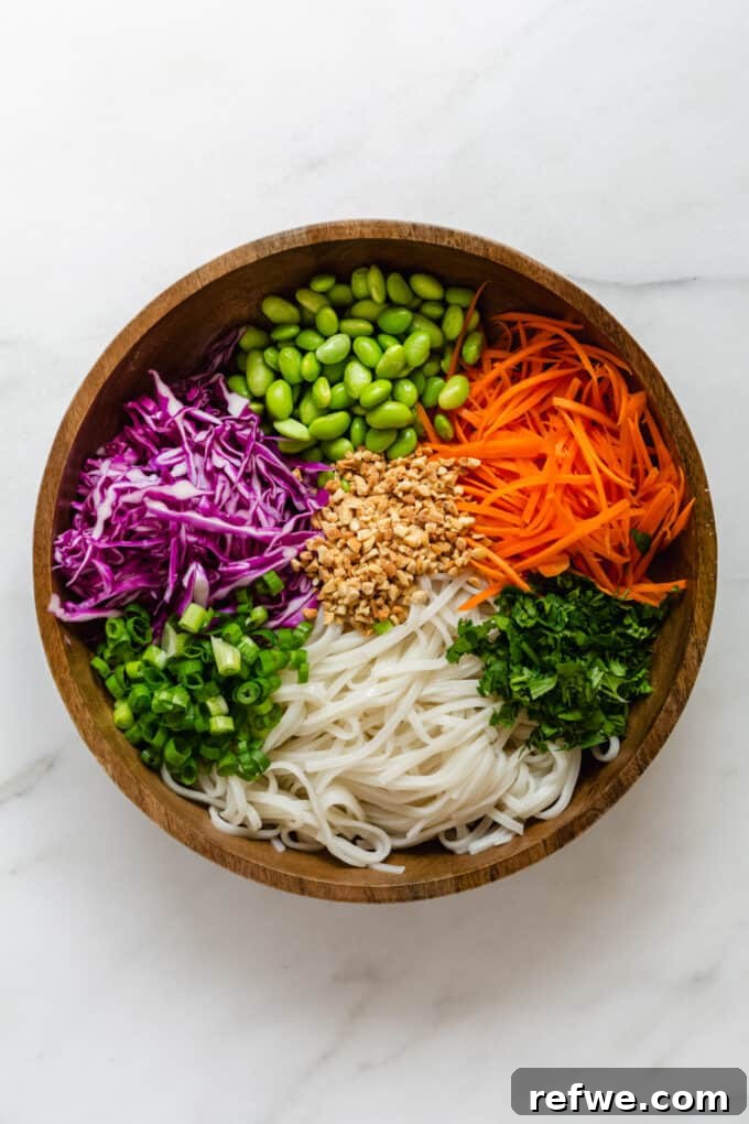 A large wooden bowl bountifully filled with freshly cooked and cooled rice noodles, vibrant shredded vegetables like carrots and cabbage, and crunchy crushed peanuts, all perfectly prepped and ready for the rich peanut dressing.