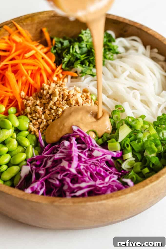 A mesmerizing stream of rich, creamy Thai peanut sauce being expertly poured from a small elegant bowl into a larger bowl of colorful Thai noodle salad, ensuring every ingredient gets perfectly coated in the irresistible dressing.