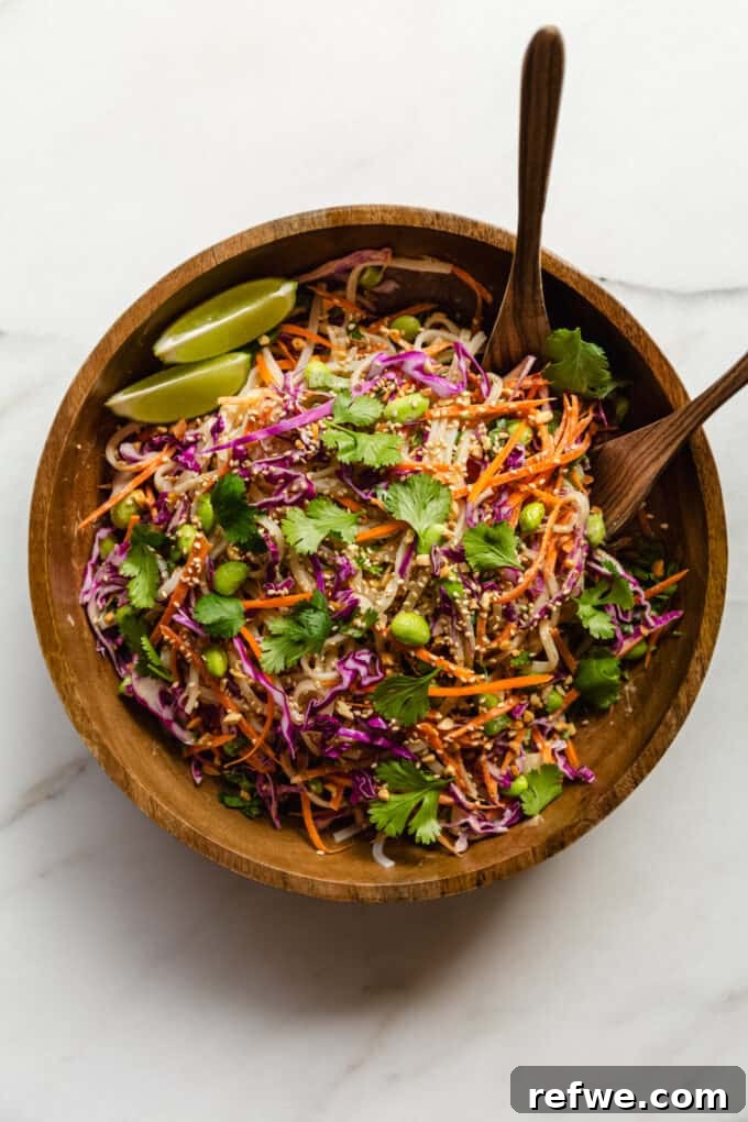 A perfectly tossed and beautifully presented Thai noodle salad, rich with creamy peanut dressing, displayed in a rustic wooden bowl with elegant wooden serving spoons, garnished with fresh herbs, ready to be enjoyed.