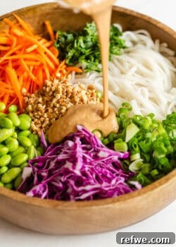 Creamy peanut sauce being poured over a colorful bowl of Thai noodle salad, emphasizing the rich texture and delicious coating for the fresh ingredients.