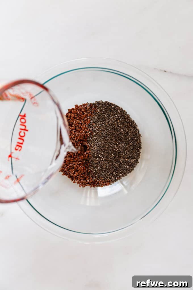 Effortless Flaxseed Crisps 4 A hand gently pouring fresh water into a clear mixing bowl containing a generous portion of flax and chia seeds, initiating the gelling process.