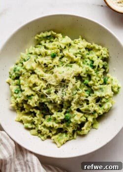 A bowl of creamy ricotta and pea pasta, garnished with Parmesan cheese and fresh basil.