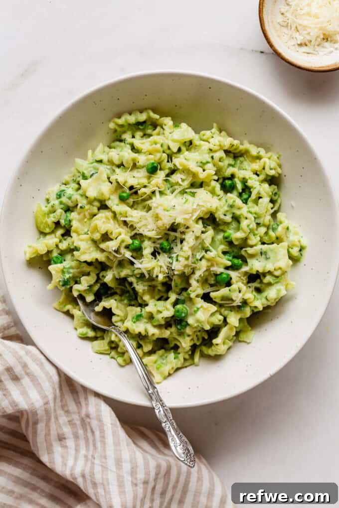 Spring Pea Ricotta Pasta 10 A beautifully plated bowl of creamy ricotta and pea pasta, garnished, with a fork and striped napkin on the side.