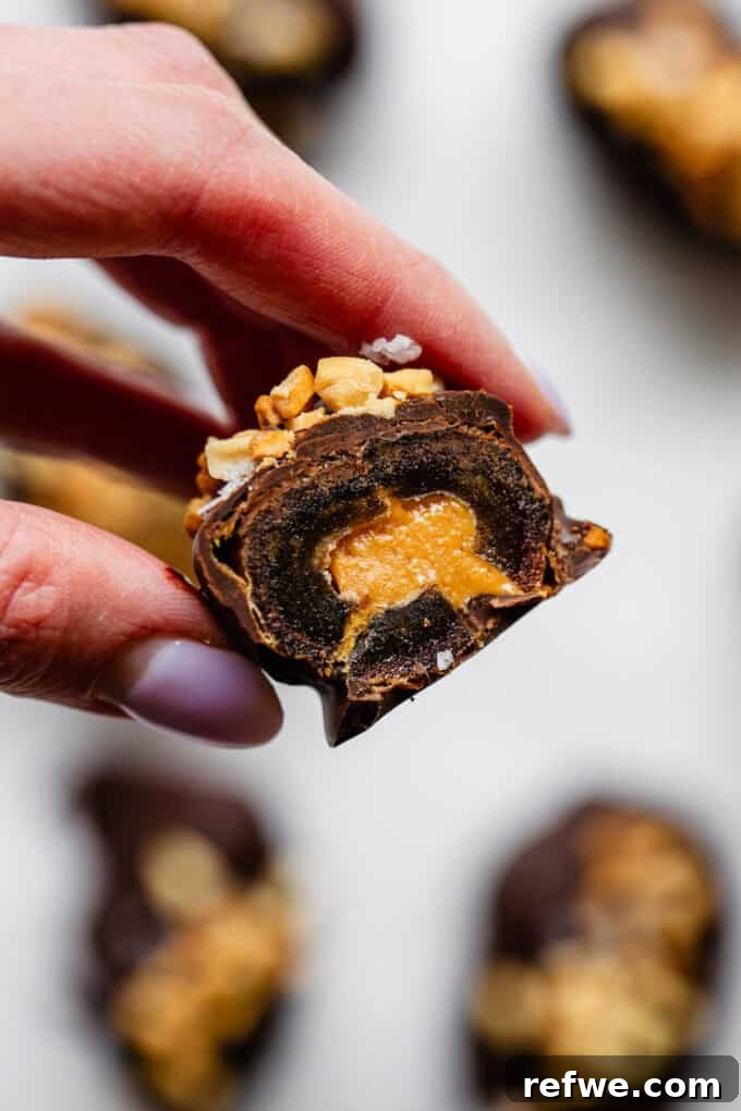 Snickers Dream Dates 10 A perfectly cut in half Snickers stuffed date, revealing its luscious layers of dark chocolate, creamy peanut butter, and chewy Medjool date interior, demonstrating its delicious cross-section.