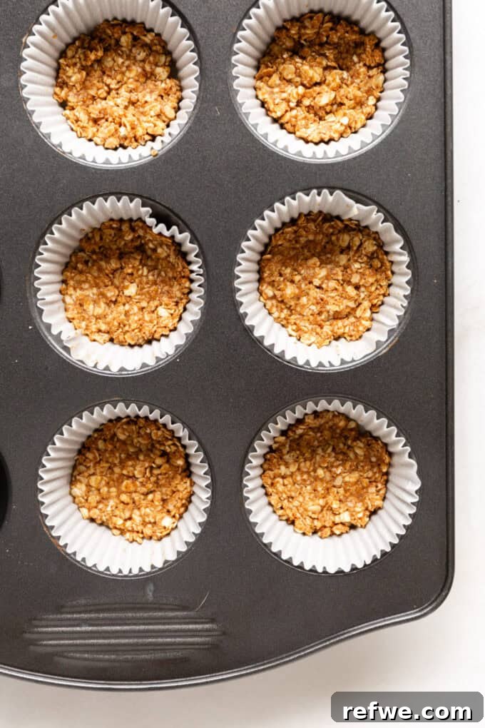Granola crust mixture firmly pressed into the bottom of a muffin tin lined with paper cups.