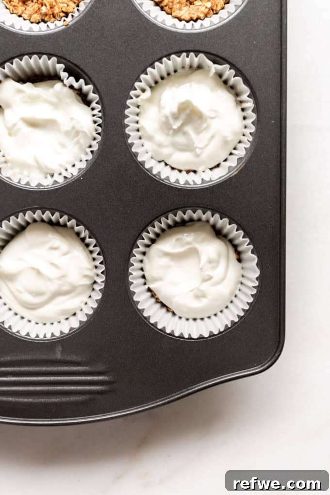 A spoonful of creamy Greek yogurt carefully added on top of the granola crust in each muffin cup.
