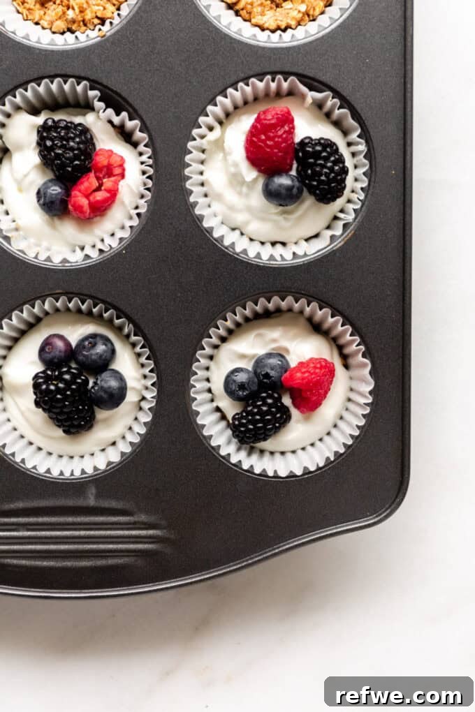 Individual granola yogurt cups in a muffin tin, topped with colorful fresh berries.