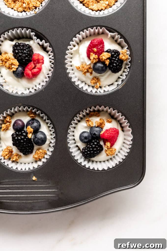A full muffin tin showcasing finished yogurt, berry, and granola cups, ready to be frozen.