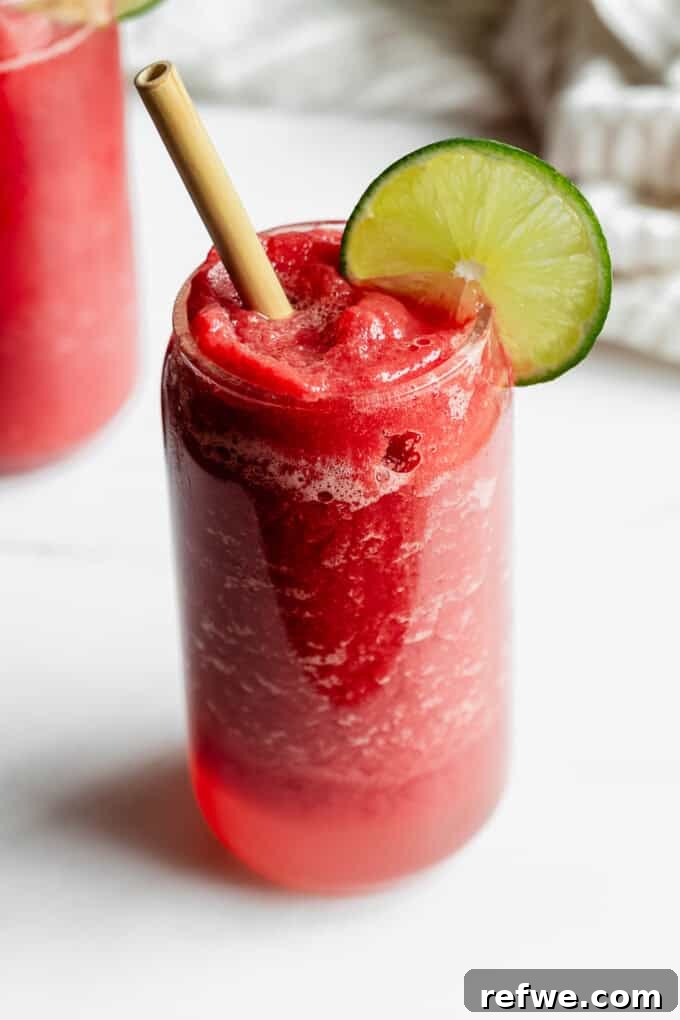 Crimson Crush 6 Two beautifully presented watermelon slushies in glasses, garnished with lime and a striped napkin, set on a modern marble counter.