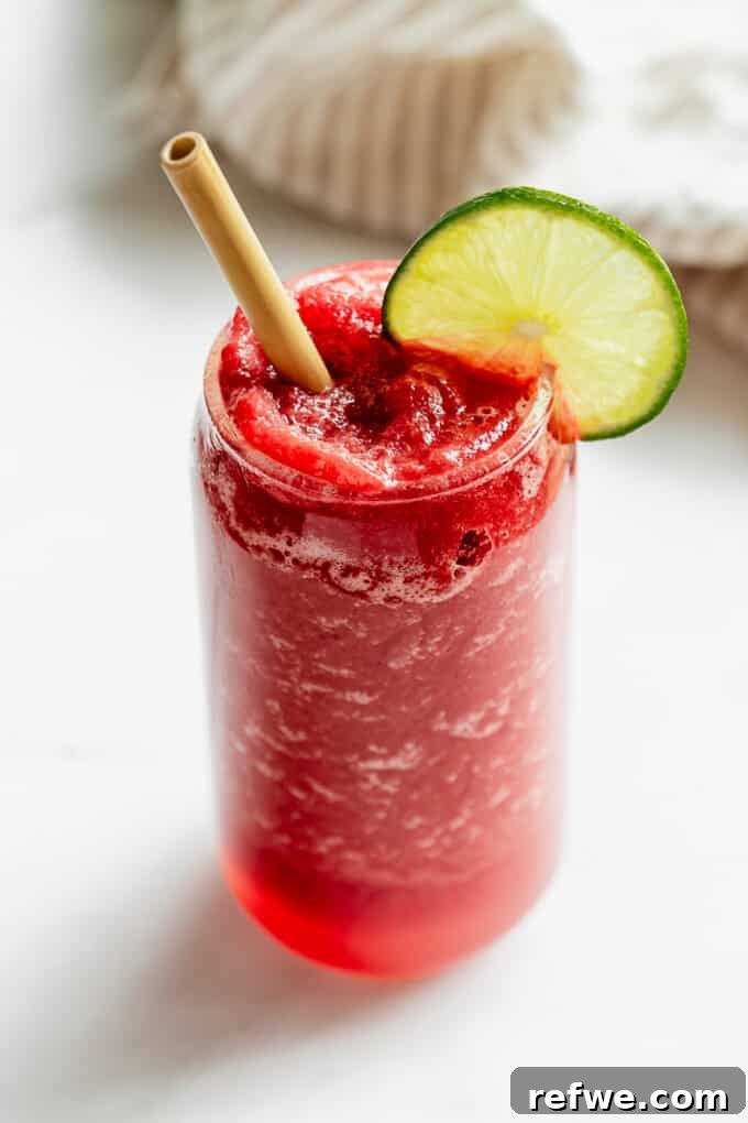 Crimson Crush 7 A single glass of a perfectly blended watermelon slushie, garnished with a lime slice and a straw, ready to be enjoyed.