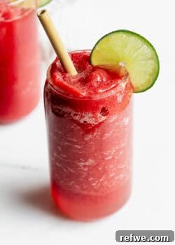 A vibrant watermelon slushie with a lime slice and bamboo straw, showcasing its refreshing appeal.