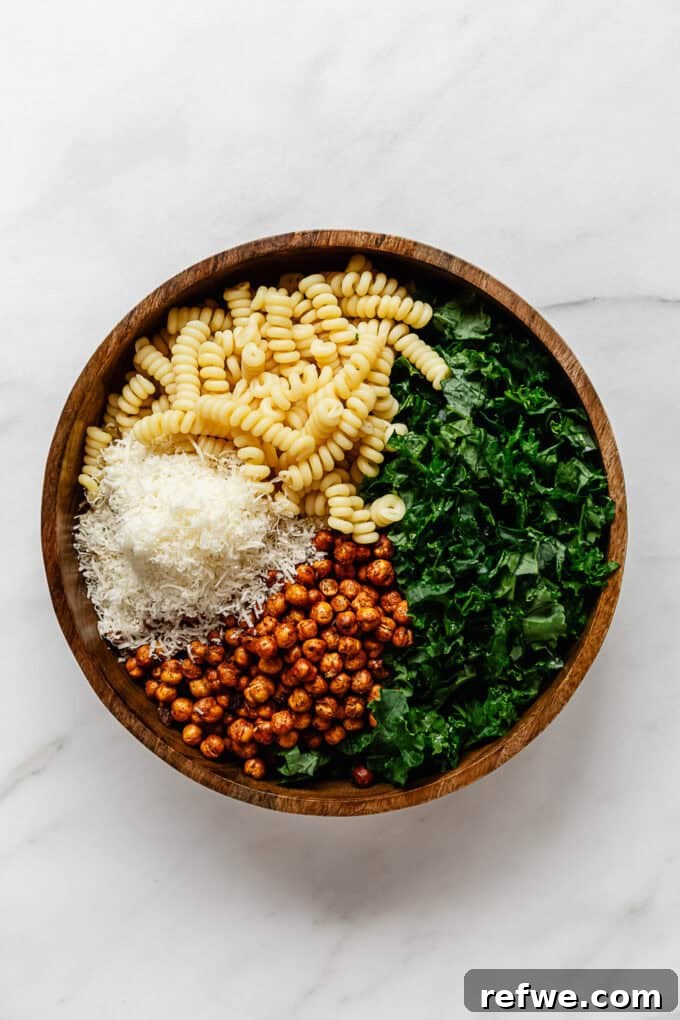 Caesar's Hearty Kale Pasta 8 A large wooden serving bowl filled with a delightful mix of kale, cooked pasta, roasted chickpeas, and grated Parmesan cheese.