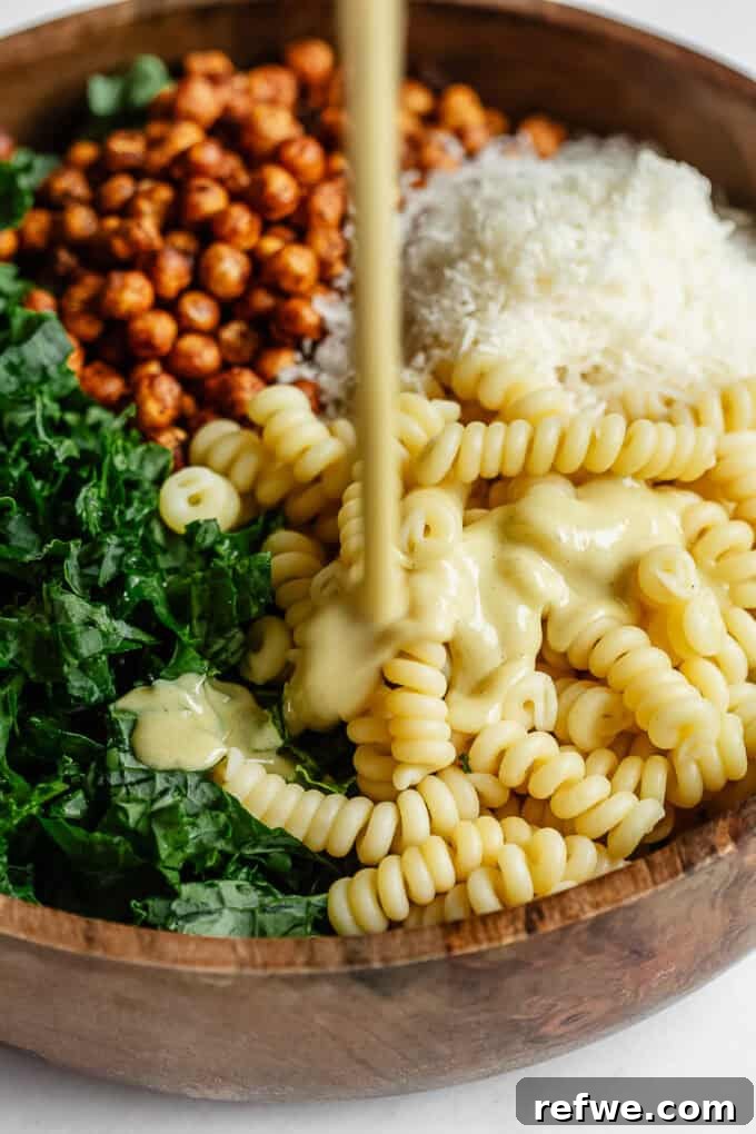 Caesar's Hearty Kale Pasta 9 Creamy Caesar dressing being poured from a jar into a bowl brimming with the kale pasta salad ingredients.