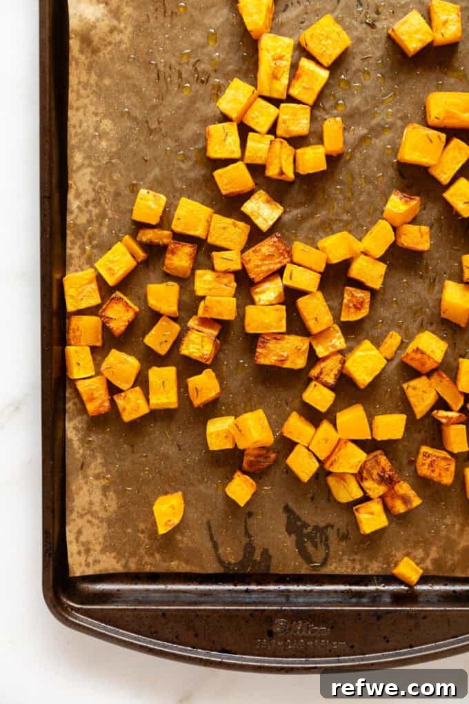Perfectly roasted and slightly caramelized butternut squash cubes on a baking sheet, golden brown and tender.