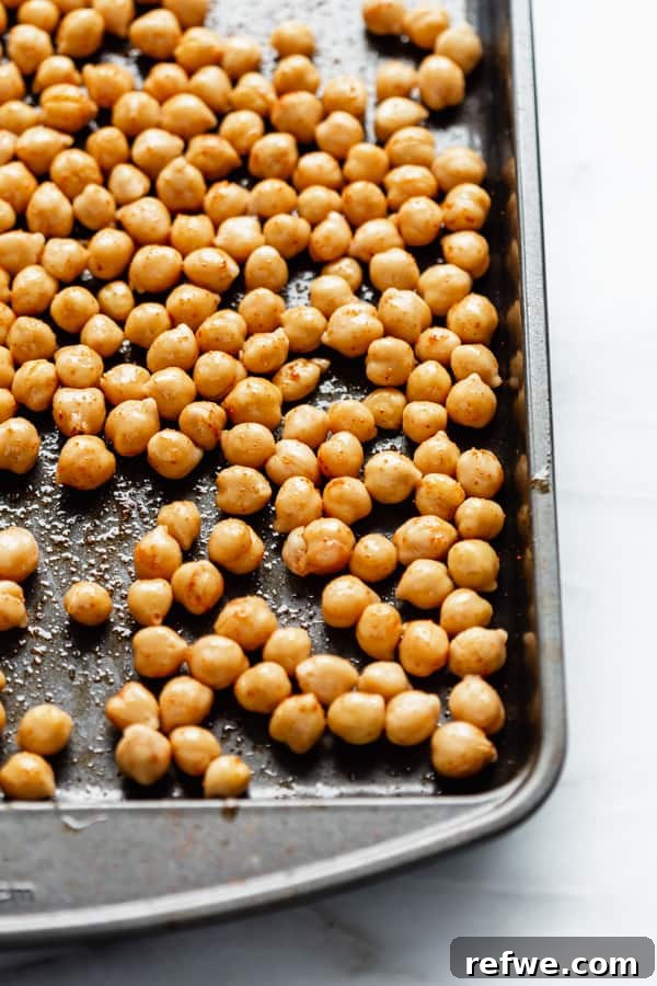 Drained chickpeas mixed with olive oil, paprika, and salt, spread on a baking tray before roasting.
