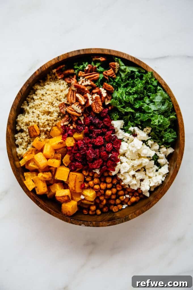 All the main ingredients of the salad – roasted butternut squash, cooked quinoa, chickpeas, crumbled feta, chopped kale, pecans, and dried cranberries – gathered in a large wooden mixing bowl.