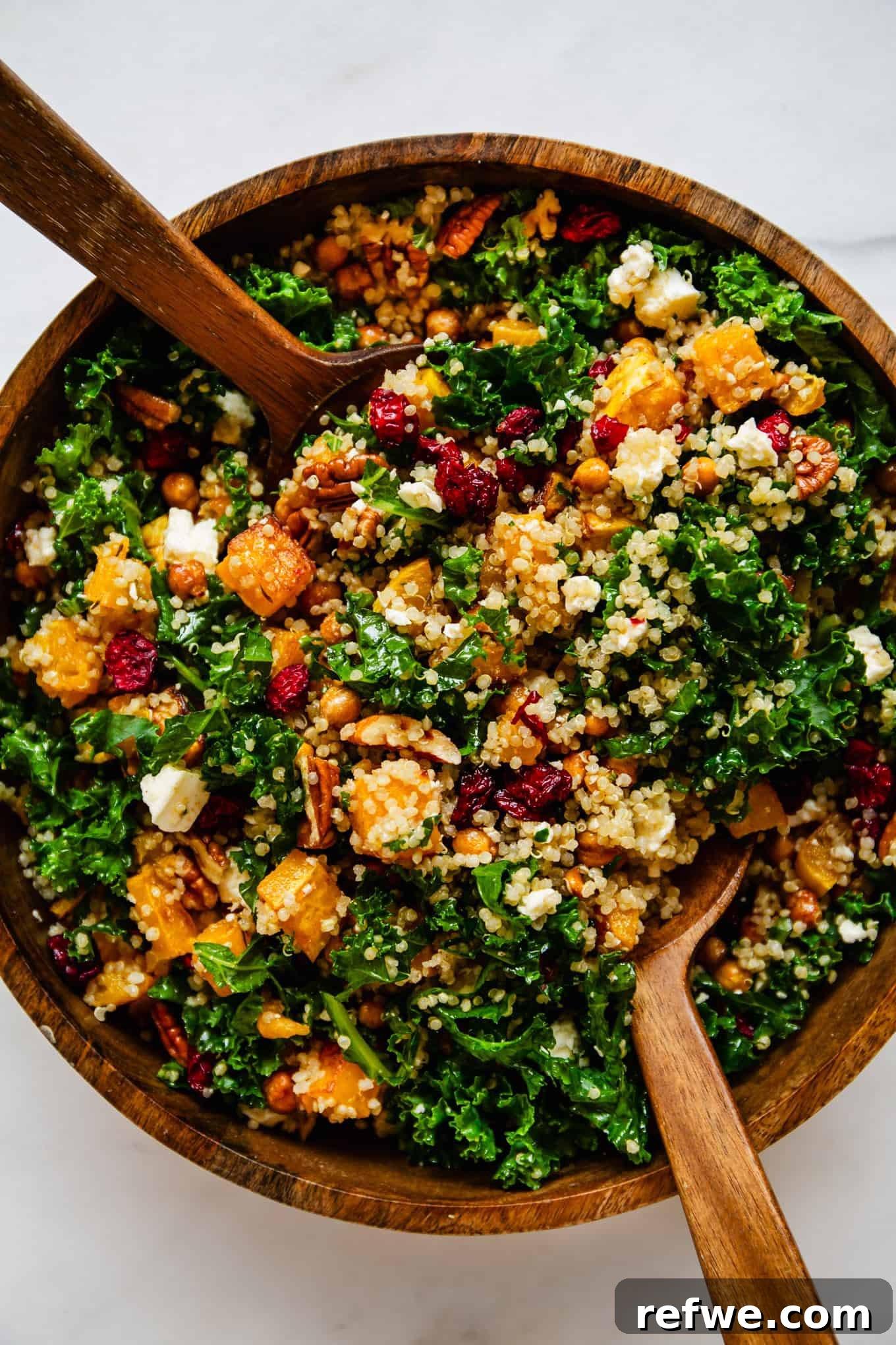 A large wooden bowl filled with the roasted butternut squash and kale salad, garnished with a pair of elegant wooden salad spoons, ready for serving.
