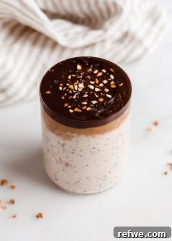 A cup of snickers overnight oats with a beige striped napkin in the back