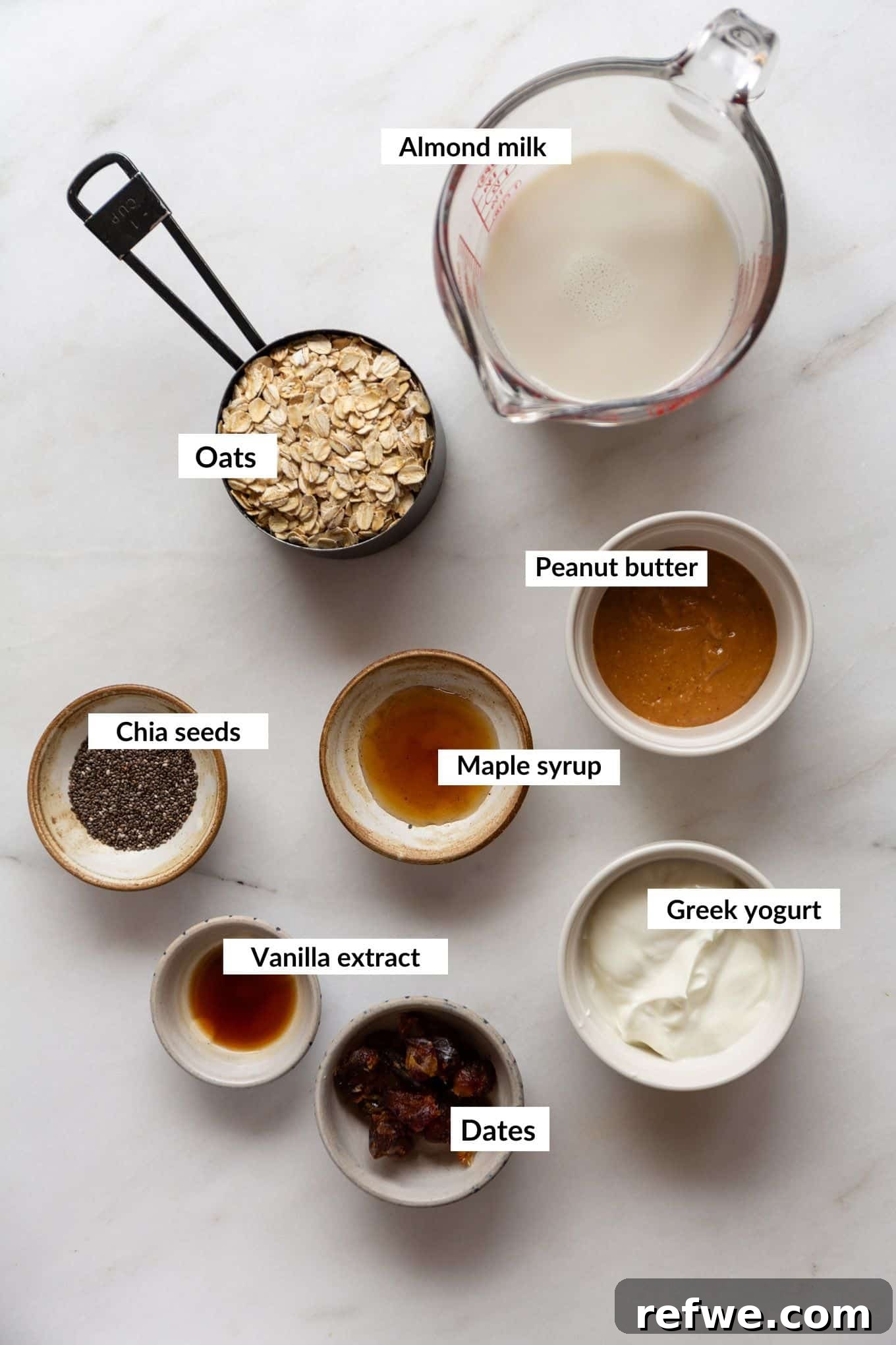 Decadent Snickers Overnight Oats 3 Collection of key ingredients for Snickers Overnight Oats including oats, chia seeds, dates, peanut butter, maple syrup, vanilla extract, Greek yogurt, and almond milk.