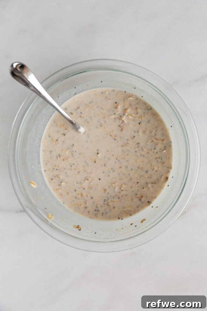 Decadent Snickers Overnight Oats 4 Un-chilled overnight oats ingredients in a clear mixing bowl with a spoon, showing the consistency before refrigeration.