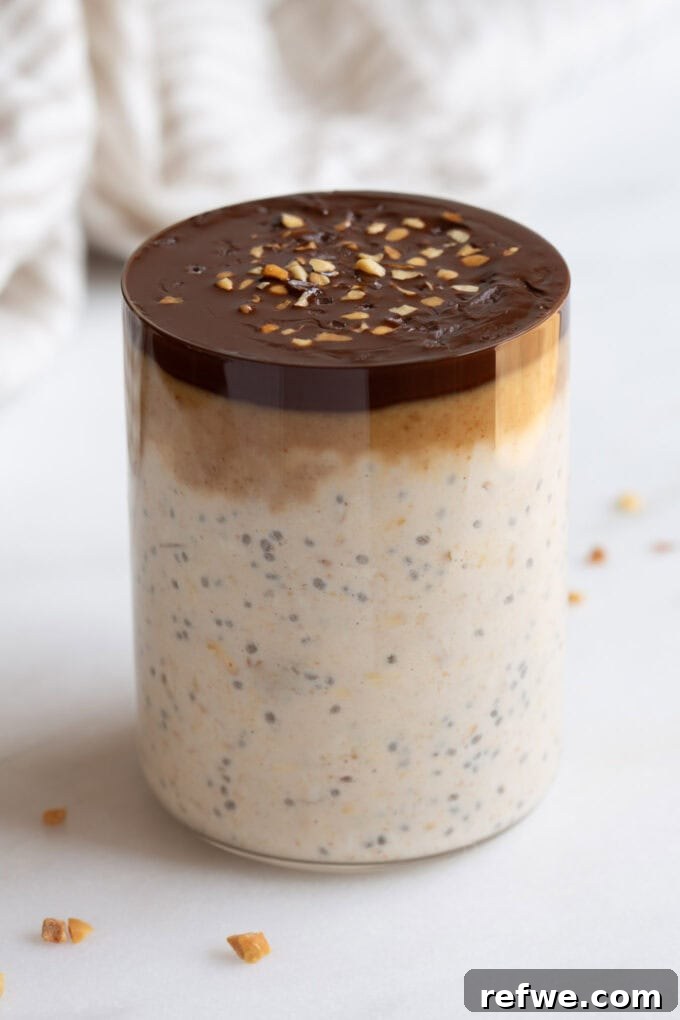 Decadent Snickers Overnight Oats 9 Assembled Snickers overnight oats in a clear cup, showing layers of oats, caramel, and chocolate shell.