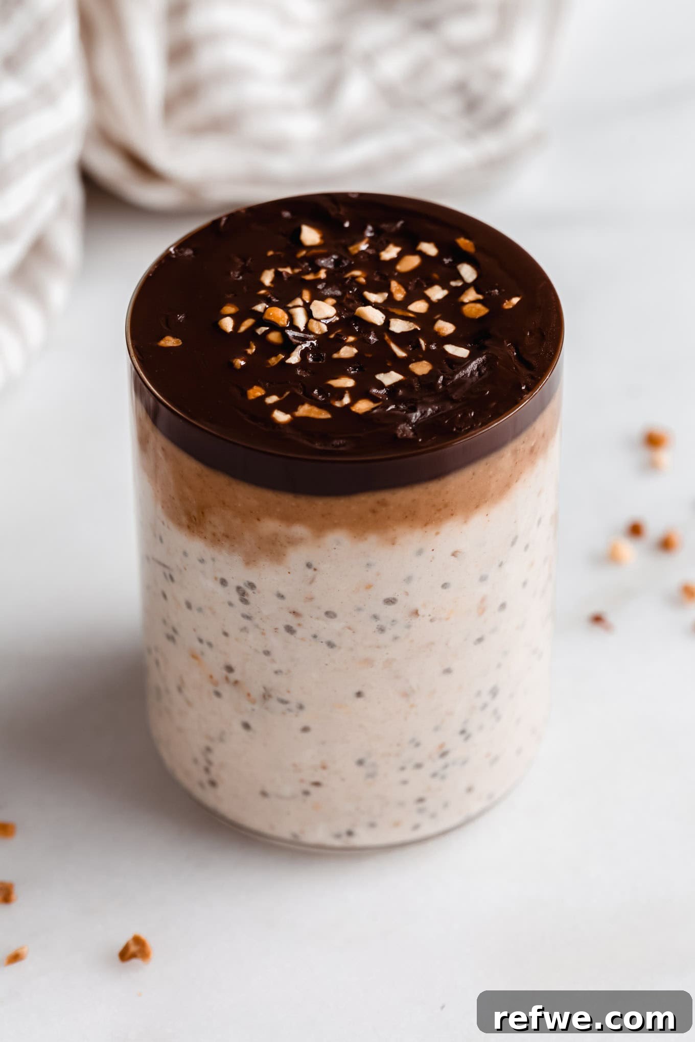 Decadent Snickers Overnight Oats 10 A beautifully presented cup of Snickers Overnight Oats, generously topped with a hardened chocolate shell and crushed peanuts for garnish.