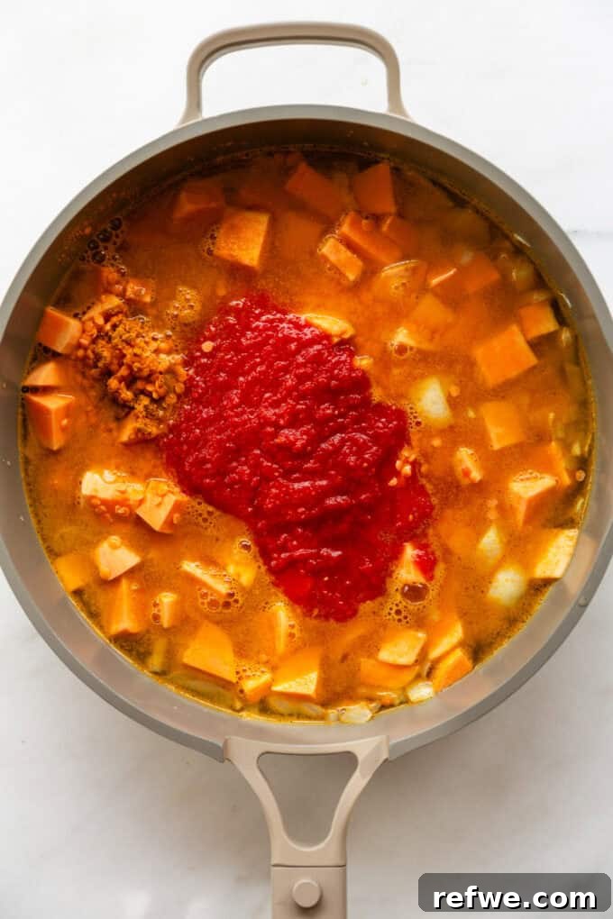 Wholesome Red Lentil Sweet Potato Curry 6 The pan now contains sweet potatoes, red lentils, vegetable broth, and crushed tomatoes, brought to a light boil and ready to simmer.