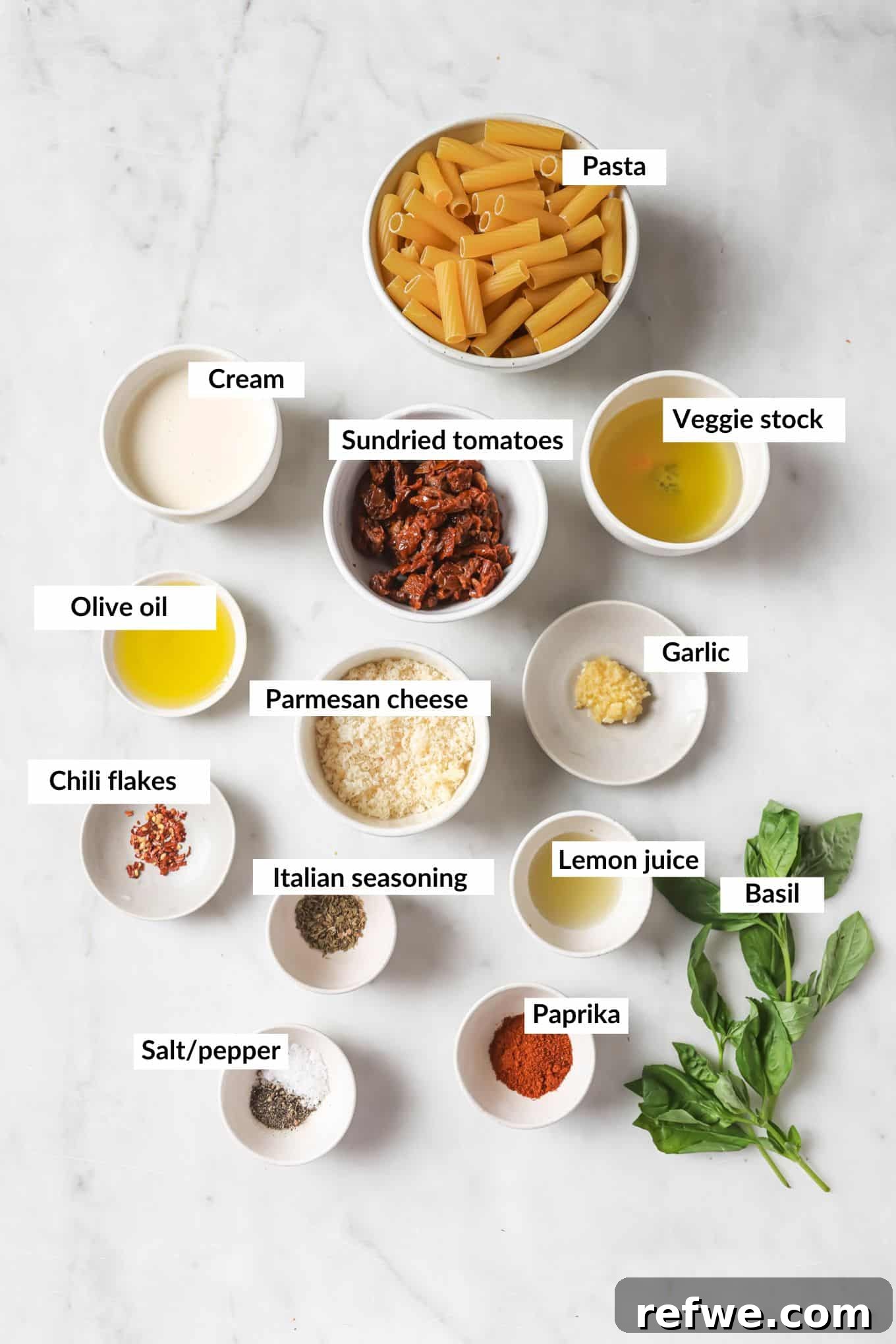 The Proposal Pasta 3 A flat lay photograph of all the key ingredients for Marry Me Pasta, including sun-dried tomatoes, garlic, heavy cream, parmesan cheese, and rigatoni, laid out on a light surface.
