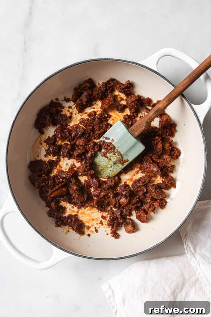 The Proposal Pasta 5 Sun-dried tomatoes and minced garlic gently sautéing in olive oil in a white skillet, releasing their fragrant aromas.