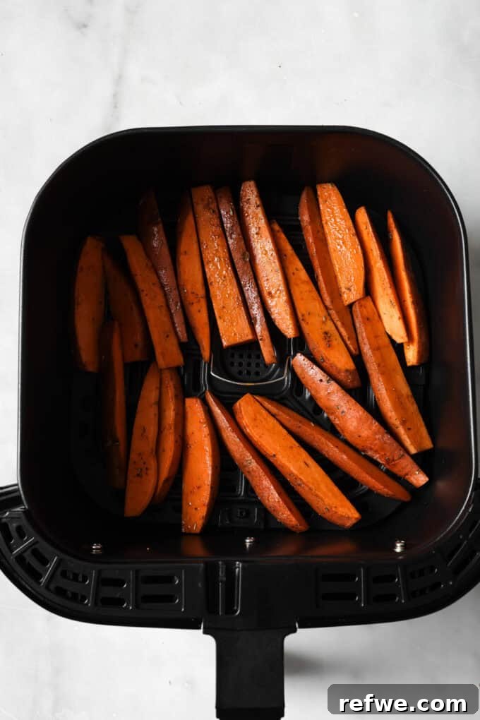 Crispy Air-Fried Sweet Potato Wedges 6 Uncooked, seasoned sweet potato wedges arranged in a single layer in an air fryer basket, ready for cooking