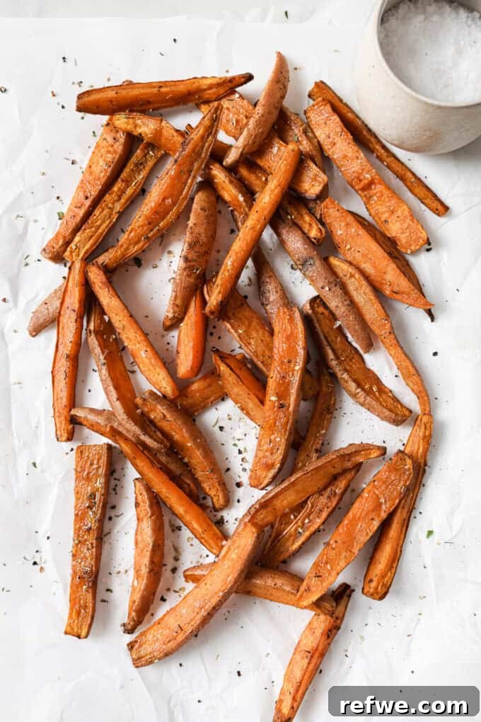 Crispy Air-Fried Sweet Potato Wedges 8 Close-up of golden-brown crispy sweet potato wedges on white parchment paper, with a small bowl of flaky salt on the side