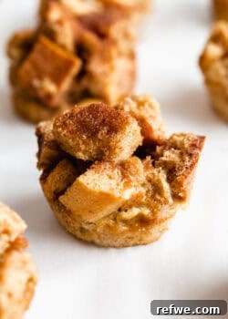 A golden-brown French toast muffin, freshly baked and topped with a sprinkle of cinnamon sugar, on a white background.