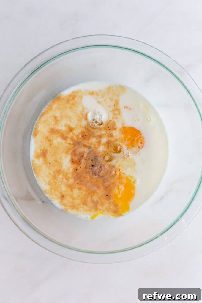 Fresh eggs, milk, and vanilla extract are carefully measured and added to a large mixing bowl.