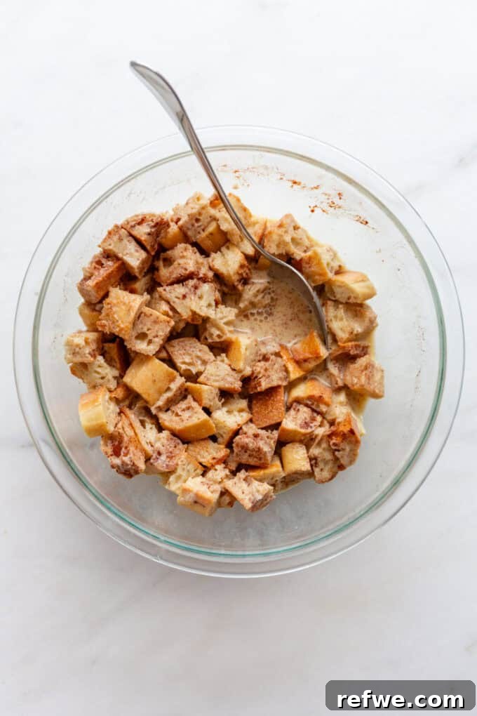Cubed bread thoroughly mixed with the egg, milk, cinnamon, and vanilla custard, soaking in the mixture within a mixing bowl.