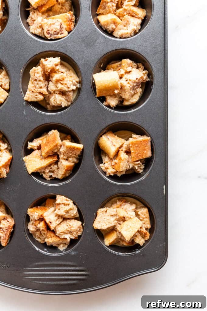 Baked French toast muffins neatly arranged in a muffin pan, golden brown and ready to be removed.